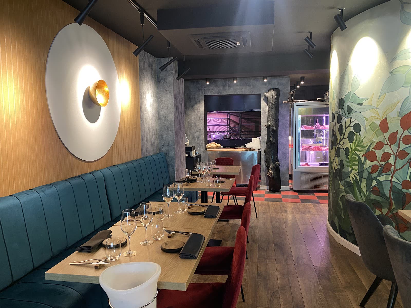 Sala lungă: banchetă teal, scaune roșii, lampă rotundă de alamă, perete cu pictură botanică